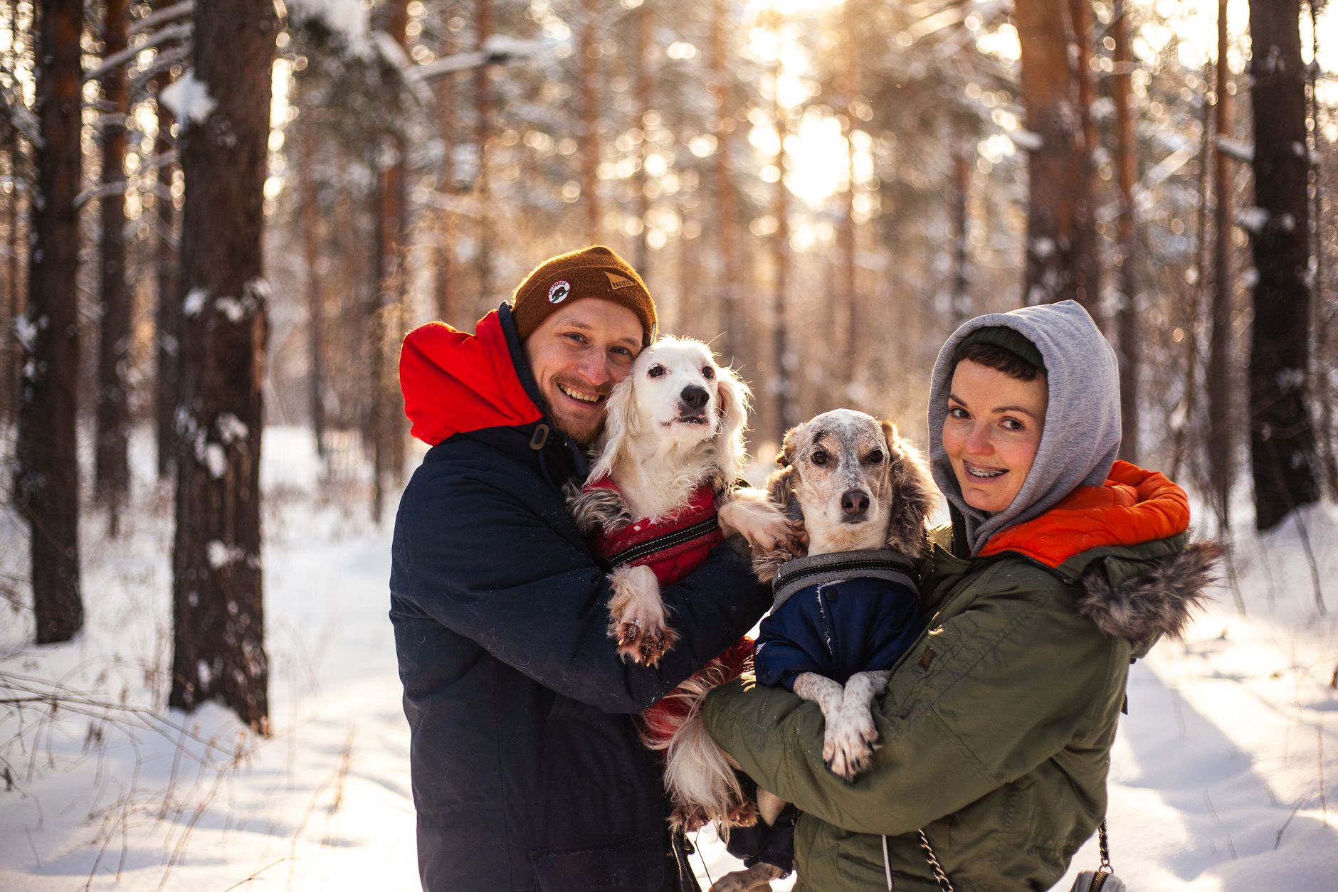 A smiling couple enjoys a winter day in the forest with their dogs.