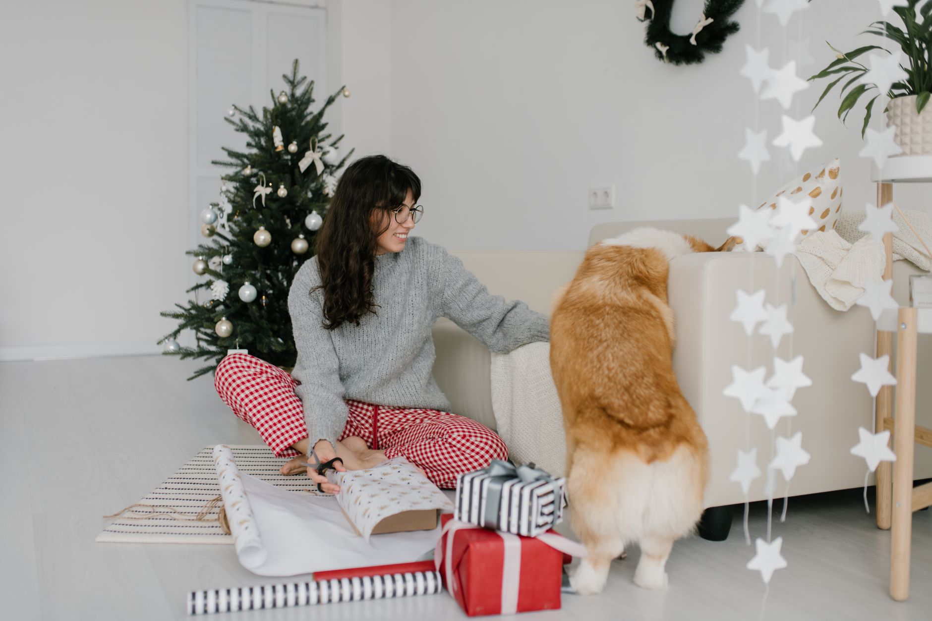 A woman and her corgi enjoying Christmas gift wrapping in a cozy living room setting.